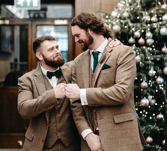 Groom with his best man wearing tweed wedding suit with green bow tie and pocket square