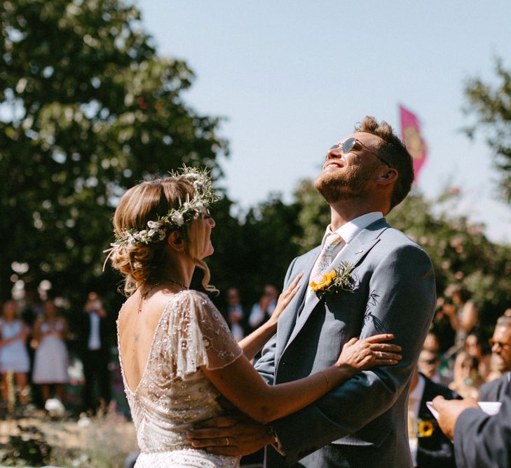 Bride in Jenny Packham Portia Wedding Dress and Groom in Grey Ted Baker Suit Laughing at Outdoor Wedding Ceremony