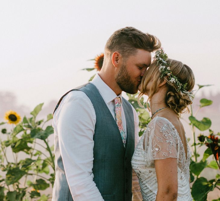 Bride in Jenny Packham Portia Wedding Dress and Flower Crown and Groom in Ted Baker Suit Kissing in a Sunflower Field