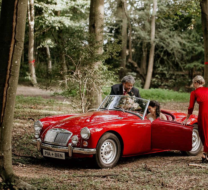 Bride arriving in a convertible red car at Evenley Wood Garden wedding