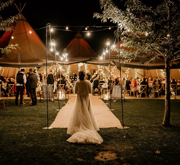 Bride in tulle skirt and wool cardigan standing outside her tipi reception at Evenley Wood Garden