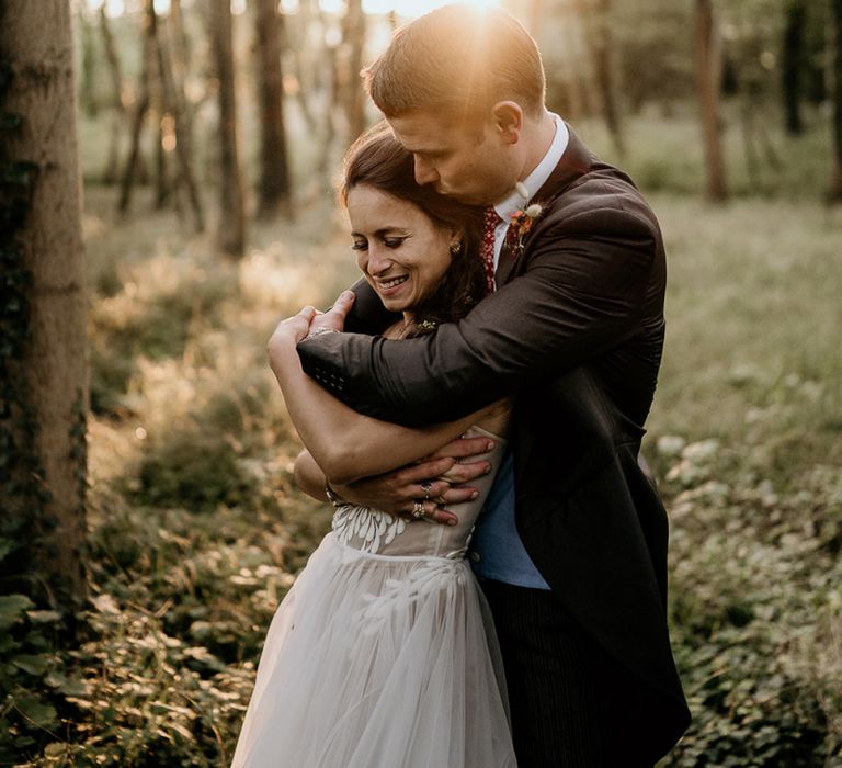 Groom embracing his bride in the woods at Evenley Wood Garden