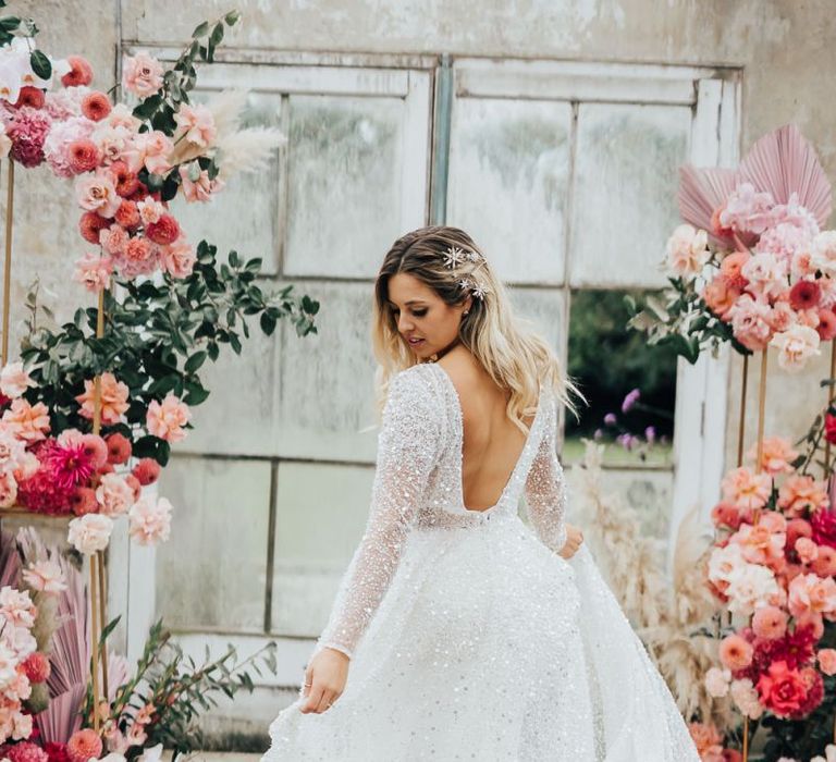 Bride in sparkling wedding dress standing in a conservatory with pink colour scheme