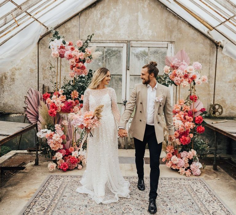 Bride and groom standing in front of a flower arrangement in pink colour scheme