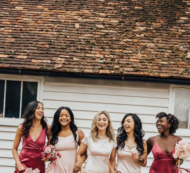 Bridesmaids walking together arm in arm in different pink dresses