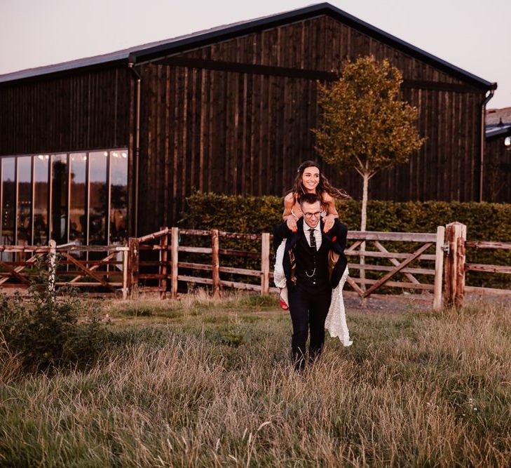 Groom Give Bride Piggy Back Through Field