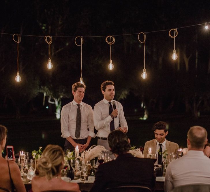 Two Grooms at Outdoor Wedding Reception Speeches with Festoon Lights | Woodland Wedding Ceremony at Sa Farinera de Sant LLuis Wedding Venue, Catalan Empordà, Spain | Planned &amp; Styled by Mille Papillons | HUMà06 Photography | HUMà06 Photography