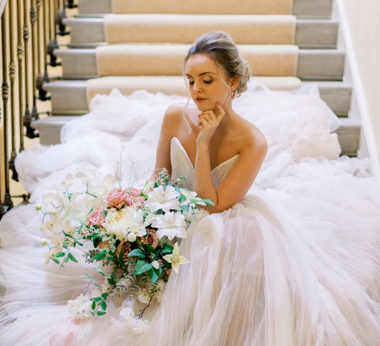 Bride in blush pink wedding dress sitting on the stairs at Prestwold Hall