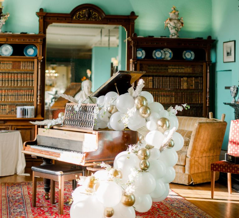 White and gold balloon arch over a grand piano