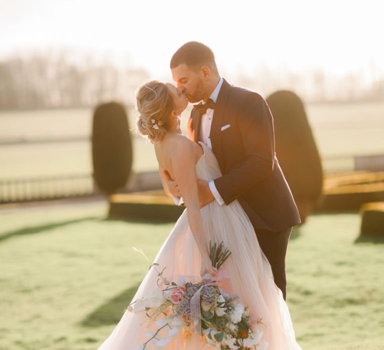 Groom in tuxedo kissing his bride in a romantic wedding dress at Prestwold Hall