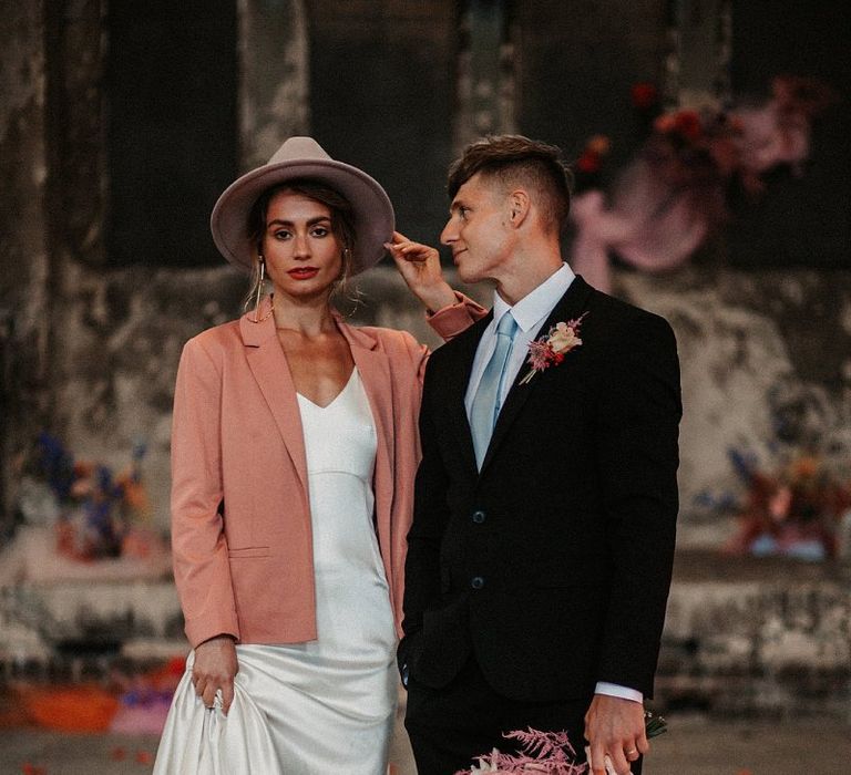 Stylish Bride and Groom in Minimalist Wedding Dress, Pink Wedding Jacket and Fedora Hat