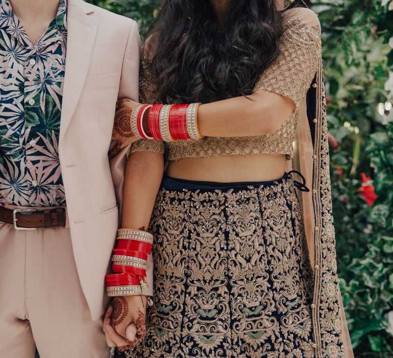 Bride in Gold and Navy Saree and Groom in Beige Suit and Floral Shirt