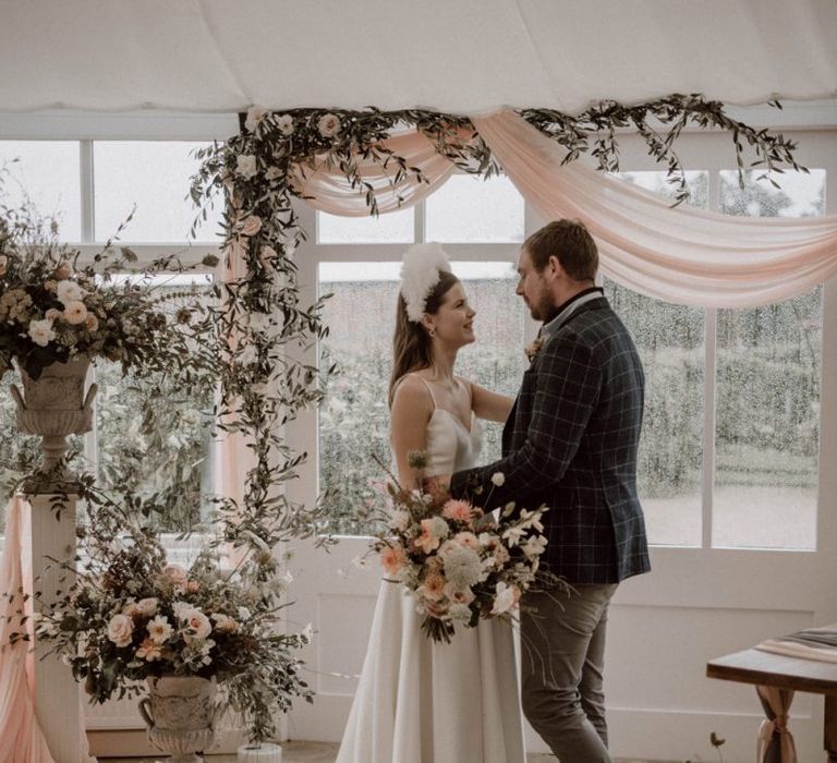 Bride and Groom Standing at the Flower Filled Altar with Pink Drapes