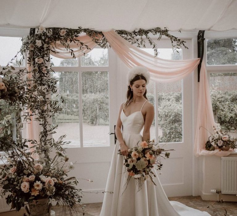 Bride in Emma Beaumont Wedding Dress with Straps Standing at the Flower and Drapes Covered Altar