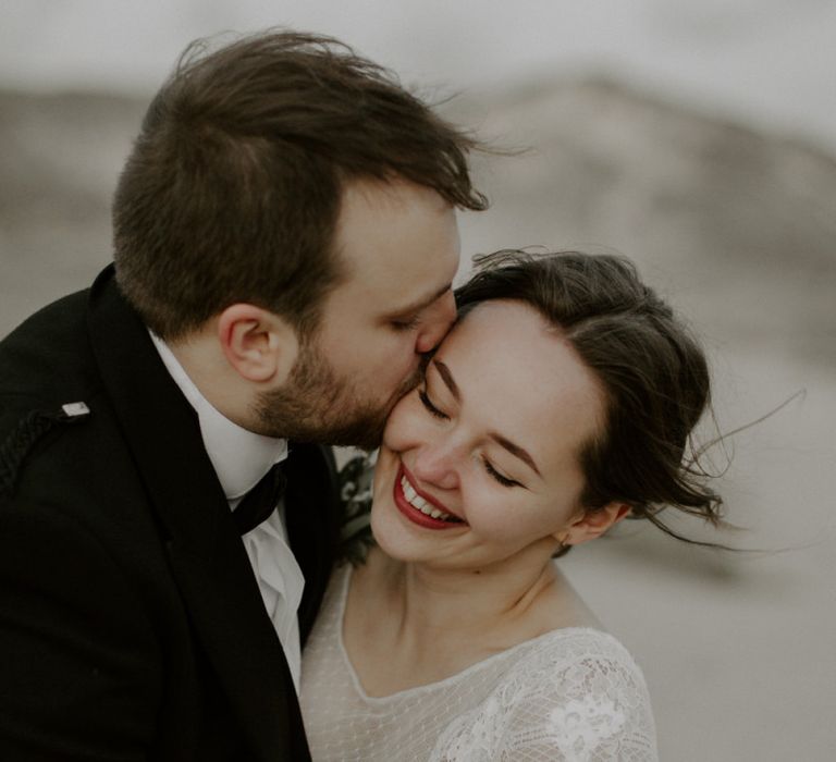 Groom Kisses Bride On Cheek During Portraits