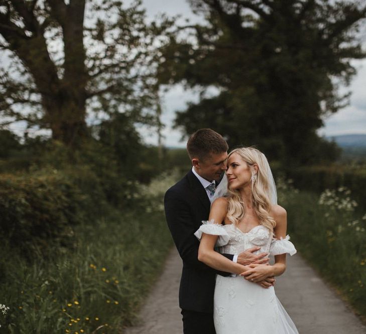 Bride in Emma Beaumont Wedding Dress and Groom Embrace In Fields