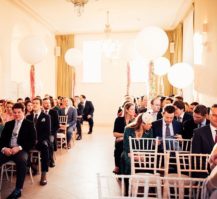 Guests wait for brides arrival below wedding balloon decor