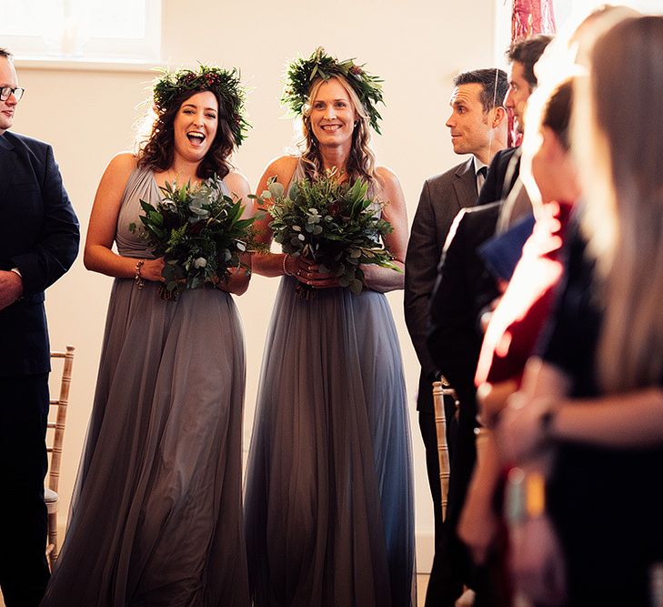 Bridesmaids in grey dresses and foliage crowns walk down the aisle