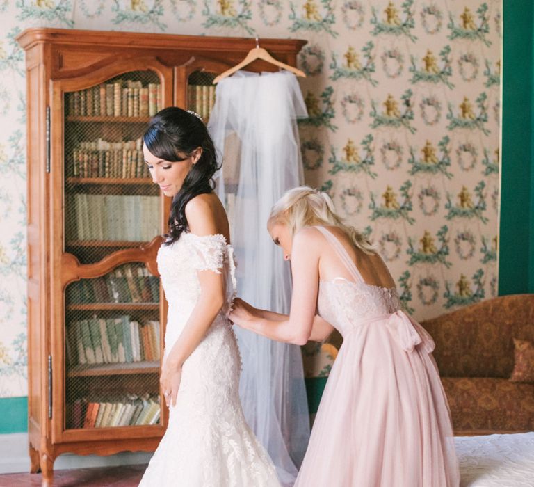 Bridesmaid in Dusky Pink Chiffon Dress Helping Bride into Her Lace David Tutera Wedding Dress