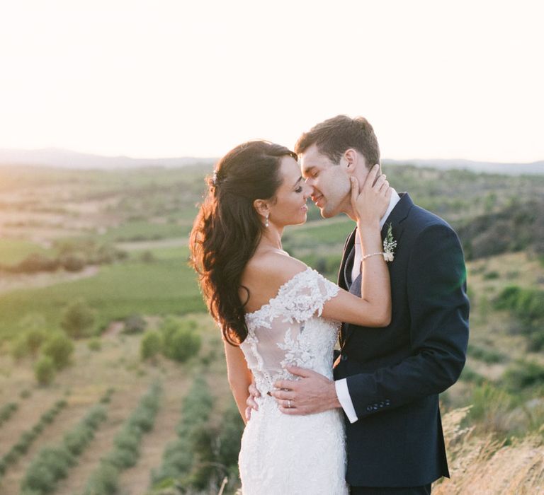 Bride in Lace David Tutera Wedding Dress and Groom in Navy Three Piece Suit  Kissing in the Mountains