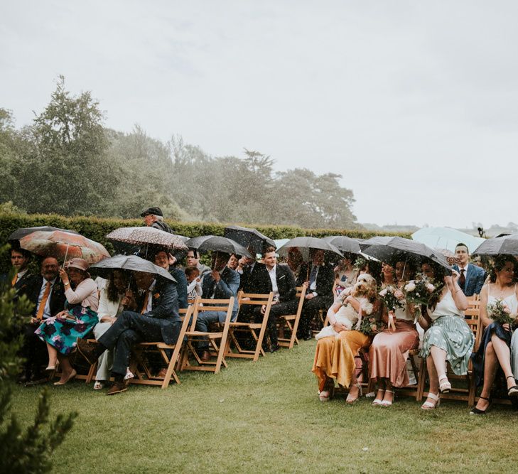 Guests huddle under umbrellas during outdoor ceremony