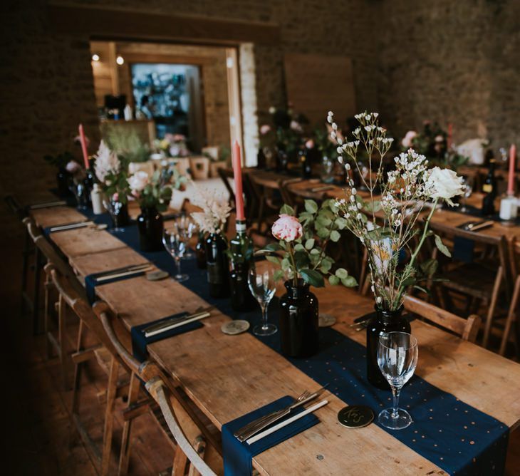 Wedding table decor with flower stems in glass bottles and navy table runners