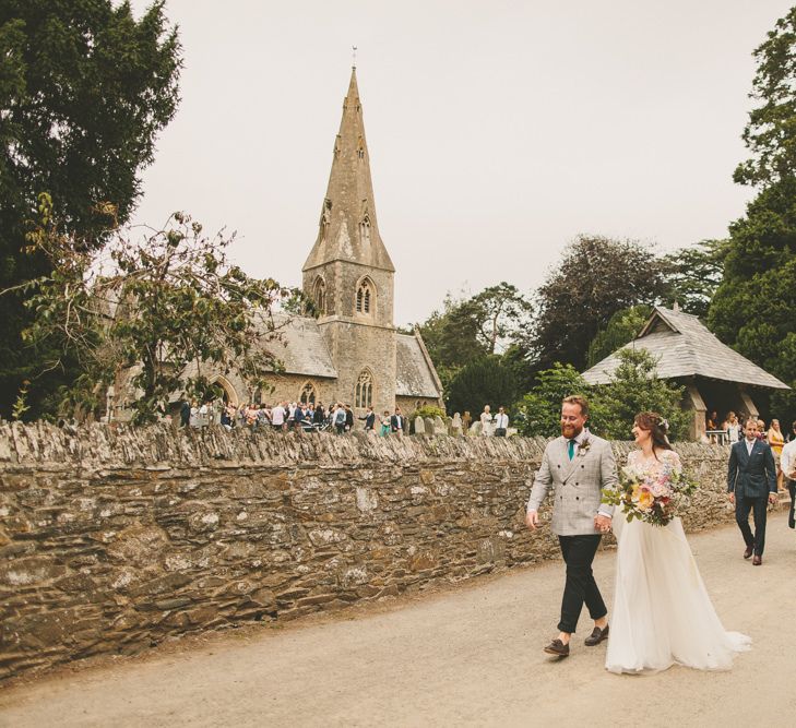 Bride and groom walk to reception with rustic decor and macrame table runner