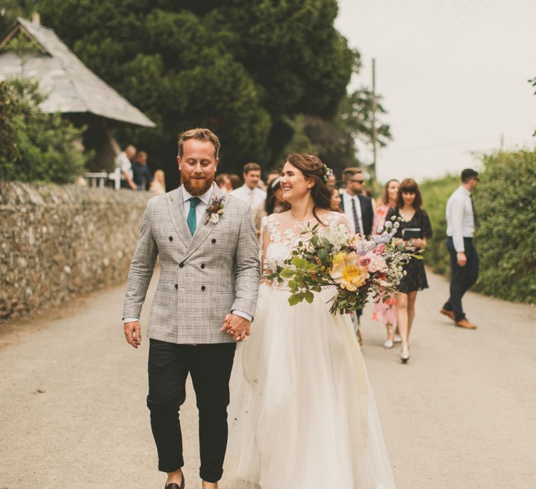 Bride and groom walk to reception with rustic decor and macrame table runner