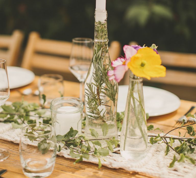 Glass bottle candle holders with foliage and macrame table runner