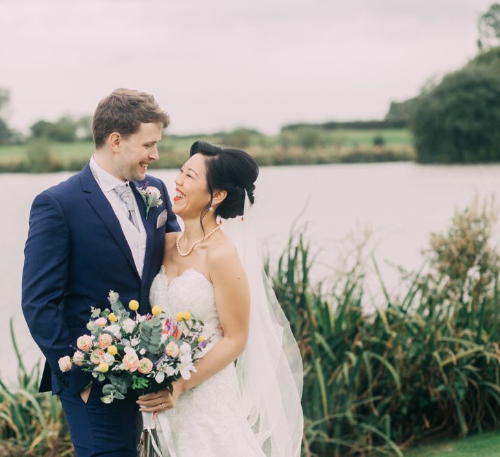 Bride and Groom Portrait by the Lake with Bride in Strapless Wedding Dress and Groom in Navy Suit