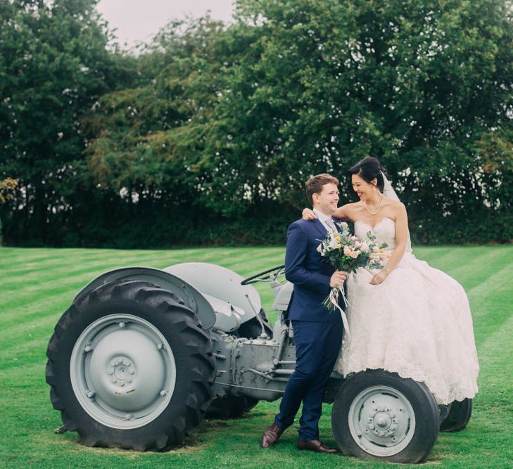 Bride in Princess Wedding Dress and Groom in Navy Suit Sitting on a Tractor