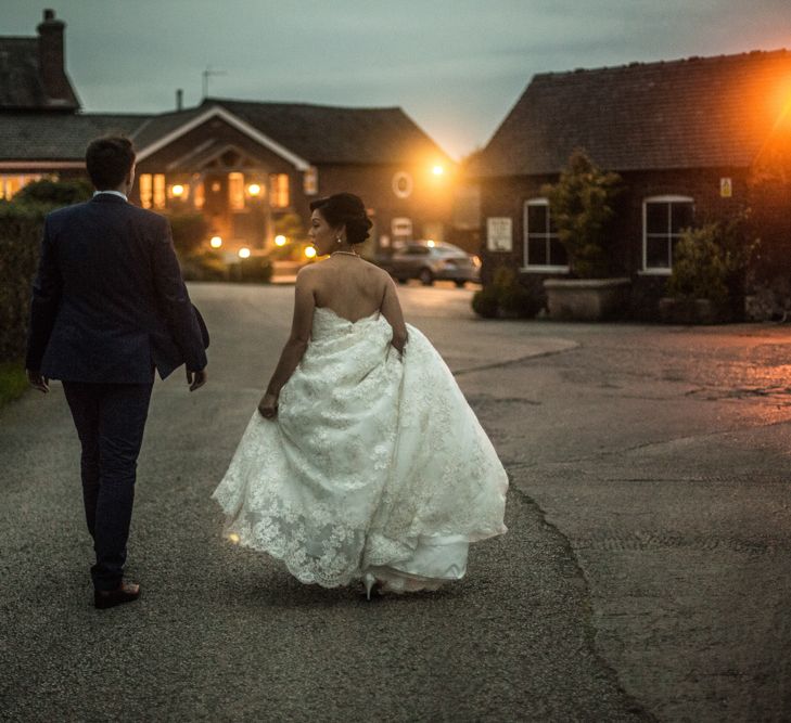 Bride in Lace Off The Shoulder Wedding Dress and Groom in Tuxedo  Walking Down a Country Lane