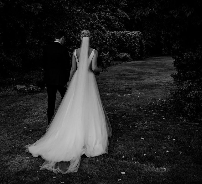 Bride in Stella York Wedding Dress and Cathedral Length Veil and Groom in Navy Suit  Walking Hand in Hand