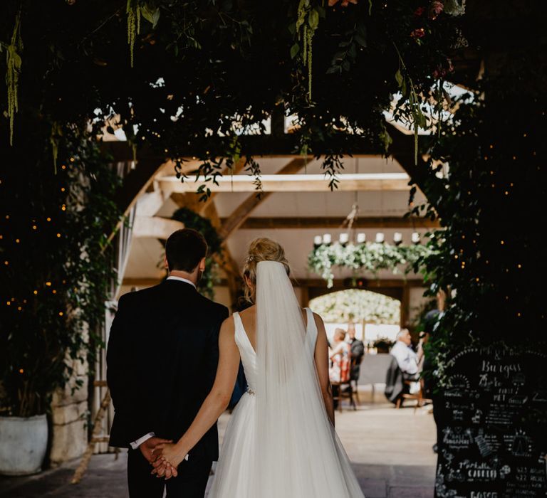 Bride in Stella York Wedding Dress with Cathedral Length Veil and Groom in Navy Wedding Suit Waiting to Enter The Wedding Breakfast