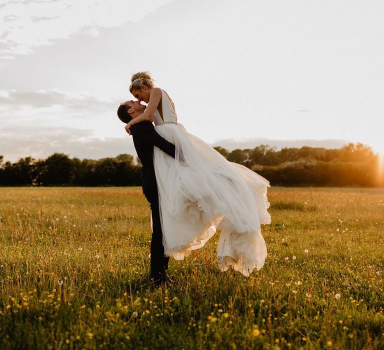 Groom in Navy Suit Lifting His Bride Up in a Stella York Wedding Dress with Tulle Skirt