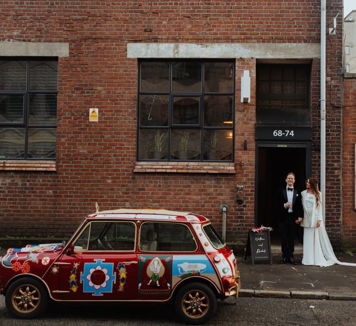 Bride and groom arrive at their reception with personalised Mini Cooper and a statement white bridal blazer