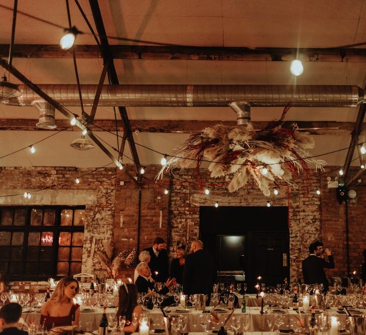 Industrial style warehouse reception with festoon lighting and a pampas grass hanging floral installation