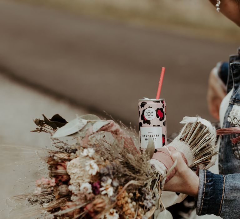 Bride holding her dried bouquet and a can of Mojito at socially distanced picnic