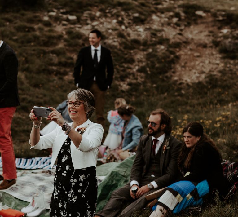 Wedding guest taking a picture on their phone at socially distanced wedding picnic