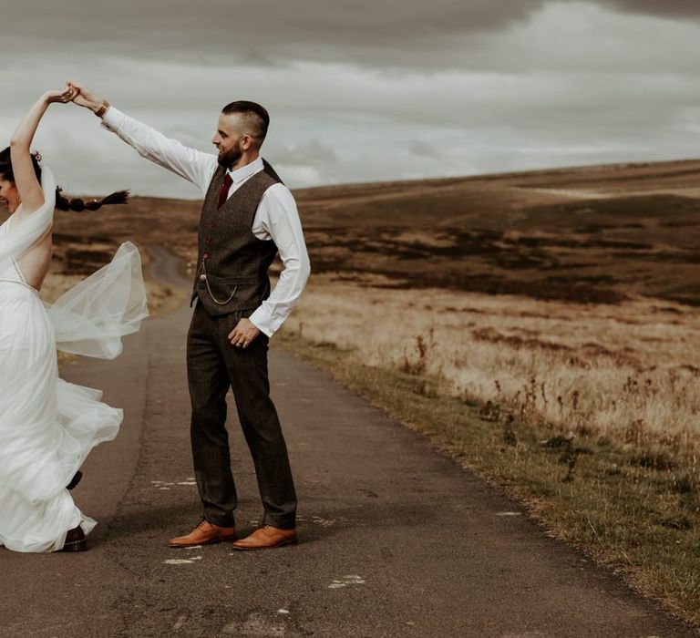 Groom in wool suit twirling his bride in Willowby Watters wedding dress