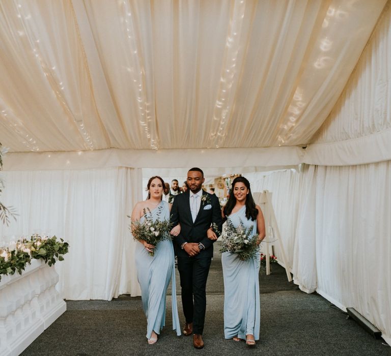 Blue bridesmaids walk up the aisle with groomsmen