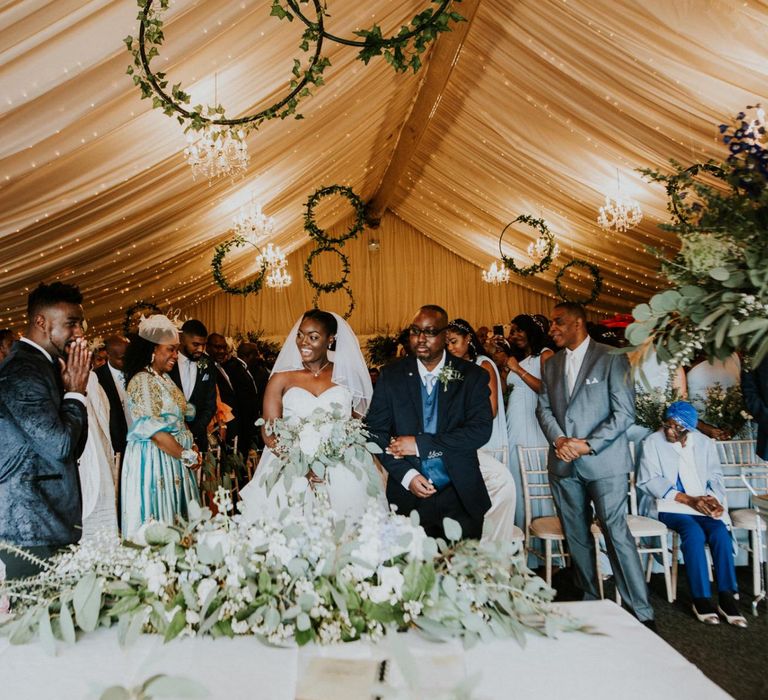 Bride and groom at marquee ceremony with wooden wedding signs and hoop decor