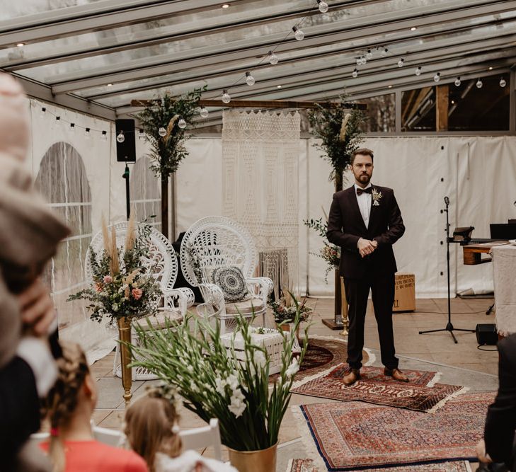 Groom in brown wedding suit waits for bride at ceremony