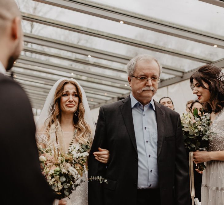 Bride walks up aisle to meet groom in brown wedding suit