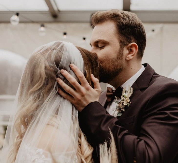 Bride in long veil greets groom in brown wedding suit