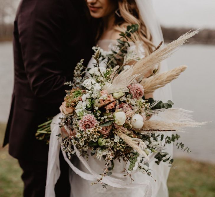 Groom in brown wedding suit with bride holding dried bouquet