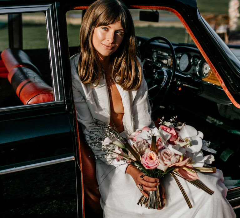 Boho Bride with Sweeping Fringe Sitting in a Wedding Car Holding a Bouquet