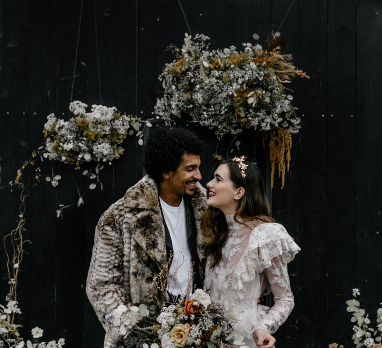 Bride in Katya Katya Wedding Dress and Groom in Faux Fur Coat Smiling at the Dried Flower Altar