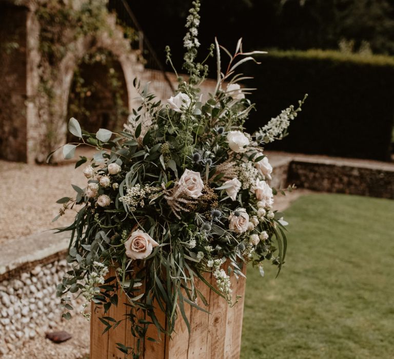 Pink rose and foliage floral arrangement on wooden plinth