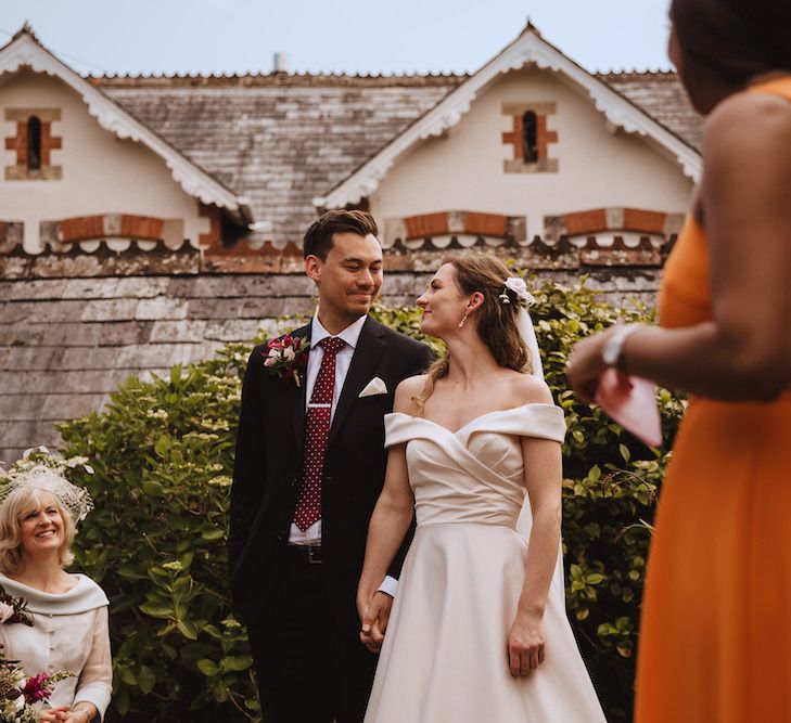 Outdoor Wedding Ceremony with Bride in Bardot Wedding Dress and Groom in Moss Bros. Suit